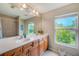 Bright bathroom with double sinks, wooden cabinets, large mirror, and a view of lush greenery from the window at 2424 Caraway Dr, Venice, FL 34292