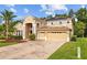 Tan two-story home boasts brick-paved driveway leading to a three-car garage at 10646 Cory Lake Dr, Tampa, FL 33647