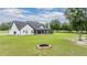 Large backyard featuring modern white home, screened porch, fire pit, green lawn, and tree line at 17566 Hyland Ln, Dade City, FL 33523