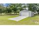 Detached metal garage with white door on a concrete slab, surrounded by lush green lawn and trees at 17566 Hyland Ln, Dade City, FL 33523
