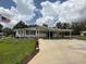 Charming single-story home featuring a long driveway, carport, and manicured lawn under a partly cloudy sky at 12021 Club House Rd, Brooksville, FL 34613