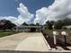 Charming single-story home featuring a long driveway, carport, and manicured lawn under a partly cloudy sky at 12021 Club House Rd, Brooksville, FL 34613
