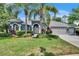 Charming blue home featuring a three-car garage, well-manicured lawn, and lush landscaping at 27440 Cedar Park Ct, Wesley Chapel, FL 33544