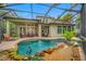 The home's backyard boasts a screened pool, outdoor living space, and lush landscaping with serene water feature at 3000 Naughton Way, Tarpon Springs, FL 34688