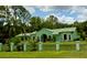 Single-story home sits behind fence and pillars amidst lush lawns and mature trees under a cloudy sky at 27752 Ravens Brook Rd, Wesley Chapel, FL 33544