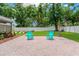 Charming brick patio with two teal chairs surrounded by a lush, green lawn and mature trees providing ample shade at 704 Childers Loop, Brandon, FL 33511