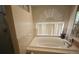 Elegant bathroom featuring a large soaking tub surrounded by beige tile and an arched window at 10402 Ashley Oaks Drive, Riverview, FL 33578