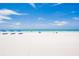 Relaxing beach scene featuring lounge chairs with blue umbrellas, white sand, and tranquil turquoise water at 17334 Gulf Blvd # 203, North Redington Beach, FL 33708