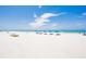 Expansive beach view featuring lounge chairs, blue umbrellas, white sand, and the turquoise Gulf of Mexico at 17334 Gulf Blvd # 203, North Redington Beach, FL 33708