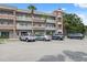 Condo building featuring a brick facade, white railings, well-maintained parking area, and lush landscaping at 2461 Rhodesian Dr # 47, Clearwater, FL 33763