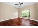 A bright bedroom with hardwood floors, a ceiling fan, and a large window offering a view of lush greenery at 5904 Pelican Bay S Plz, Gulfport, FL 33707
