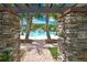 View of a community pool through a stone archway, framed by manicured landscaping and palm trees at 4155 Barletta Ct, Wesley Chapel, FL 33543