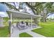 Outdoor kitchen with two grills, picnic tables, and a white roof in a grassy area with mature trees at 4801 Airport Rd # 211, Zephyrhills, FL 33542