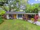 Charming single-story home with mature trees, colorful plants, carport, and bright yellow front door at 1311 W Perdiz St, Tampa, FL 33612
