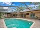 Inviting screened-in pool area with brick pavers, outdoor television, and lush tropical landscaping creating a backyard oasis at 1695 Cinnamon Ln, Dunedin, FL 34698
