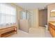 Bright bathroom features a glass enclosed shower, white tile floor, and wooden bench by the window at 17527 Stinchar Dr, Land O Lakes, FL 34638