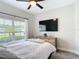 Bright bedroom with a large TV, a ceiling fan, and a window overlooking the neighborhood at 18079 Romanesque Ct, Spring Hill, FL 34610