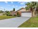 View of the house's brick facade, grey driveway, and manicured yard with a mature palm tree under a partly cloudy sky at 326 Circle Dr, Palm Harbor, FL 34683