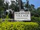 Community entrance sign for Woodside Village Condominiums amid lush, manicured landscaping at 4215 E Bay Dr # 1707C, Clearwater, FL 33764