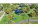 Aerial view of a playground with shaded play equipment, surrounded by palm trees and green turf for safe play at 9115 Panda Ln, Port Richey, FL 34668