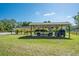 Side view of a three-car carport with several vehicles parked underneath, a spacious yard, and mature trees at 3452 Forelock Rd, Tarpon Springs, FL 34688