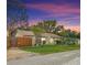Charming home boasts a well-manicured lawn, mature trees, and a warm, inviting exterior at dusk at 6425 S Adelia Ave, Tampa, FL 33616