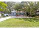 Quaint one-story home featuring mature trees, vibrant green grass, and a welcoming red railing entrance at 715 W 109Th Ave, Tampa, FL 33612