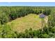 Aerial view of a modern farmhouse on expansive green field surrounded by tall trees under clear blue skies at 4261 Burns Rd, Brooksville, FL 34602