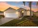 Charming single-story home featuring a two-car garage, arched entryway, and lush landscaping, set against a vibrant sunset sky at 4411 Whitton Way, New Port Richey, FL 34653