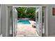 A bright patio, seen through open French doors, has a rectangular pool, stone pavers, and a view of lush trees at 719 58Th S St, Gulfport, FL 33707