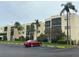 Exterior view of a multi-story building with a red car in the parking lot and tropical landscaping at 11485 Oakhurst Rd # 1200-214, Largo, FL 33774