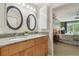 Bright bathroom features a double sink with granite countertop, oval mirrors, and a glimpse into the bedroom at 18914 Geraci Rd, Lutz, FL 33548