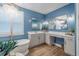 A modern blue bathroom features a soaking tub, double vanity, and decorative light fixtures at 2388 Oakwood Preserve Dr, Wesley Chapel, FL 33543