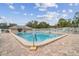 Community pool surrounded by a brick deck, a building, a white fence, and trees on a sunny day with blue sky at 13127 Topflite Ct, Hudson, FL 34669