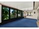 Enclosed sun room with large windows and blue carpet flooring provides a relaxing space to enjoy the outdoors from inside at 10407 Oleander Dr, Port Richey, FL 34668