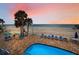 View of the pool with beach chairs and umbrellas with the beach and ocean in the background at 24 Gulf Blvd # 1C, Indian Rocks Beach, FL 33785