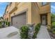 Exterior view of a tan townhome with a brown garage door, a welcoming entrance, and landscaped surroundings at 6031 Grand Sonata Ave, Lutz, FL 33558