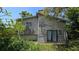 The back exterior of the home displays overgrown foliage and access to yard at 1107 Goshen Rd, Tarpon Springs, FL 34689
