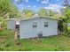 Back exterior featuring light blue paint, lush grass, and large trees at 1807 E Bougainvillea Ave, Tampa, FL 33612