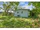 Back exterior featuring light blue paint, lush grass, and large trees at 1807 E Bougainvillea Ave, Tampa, FL 33612