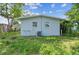 Back exterior featuring light blue paint, lush grass, and large trees at 1807 E Bougainvillea Ave, Tampa, FL 33612