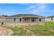 Rear exterior featuring a covered patio, neutral color palette, and a well-manicured lawn at 5441 Chestnut Ridge Rd, Dade City, FL 33523