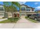 Three-story townhome with a two-car garage, manicured lawn, mature trees, and a large, concrete driveway at 11526 Crowned Sparrow Ln, Tampa, FL 33626