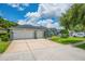 A wide driveway leads to a light gray house with a dark roof, large garage and beautiful landscaping at 15309 Palomapark Ln, Lithia, FL 33547