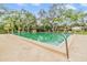Serene community pool surrounded by mature trees and lounge seating under a blue sky at 2699 Seville Blvd # 207, Clearwater, FL 33764