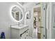 Well-lit bathroom featuring a round illuminated mirror, a modern vanity, and an open doorway to another room at 5728 14Th N Ave # 101B, St Petersburg, FL 33710