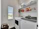 Bright laundry room with modern washer and dryer, open shelving, and a large window overlooking the backyard at 6512 Simone Shores Cir, Apollo Beach, FL 33572