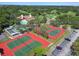 Aerial view showcasing tennis courts, pool, and surrounding green landscape with a clubhouse in the background at 12101 Meadowbrook Ln, Hudson, FL 34667