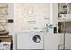 Well-lit laundry room featuring white washer and dryer with storage shelving, a decorative light fixture, and inspiring wall art at 4926 Pennecott Way, Wesley Chapel, FL 33544