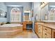 Bright bathroom with a soaking tub, tiled steps, vanity, and a large arched window for natural light at 17203 Talence Ct, Tampa, FL 33647